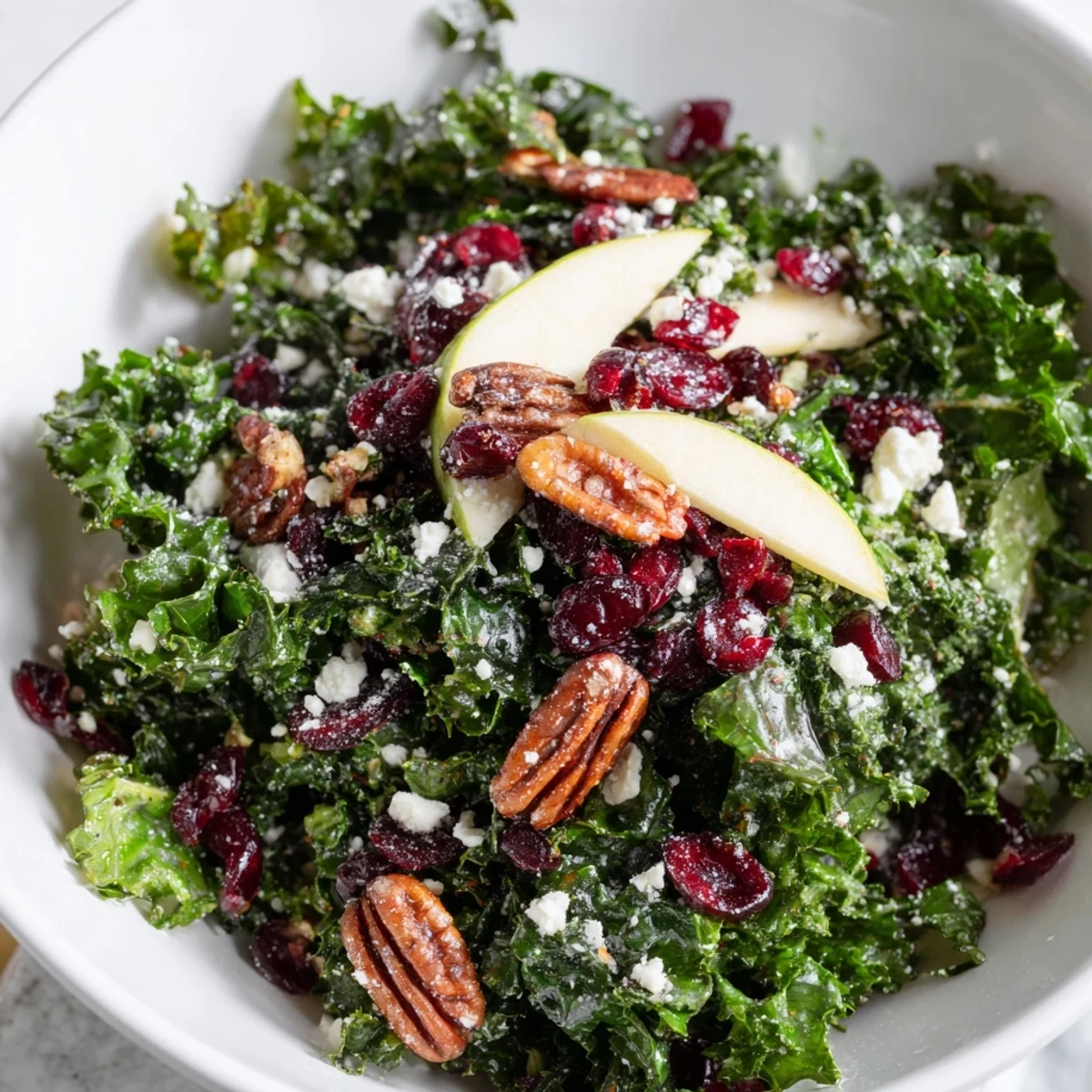 A close-up of Winter Kale Salad with Dried Cranberries, showing massaged kale leaves, sweet fruit, and crunchy nuts on a rustic wooden table.