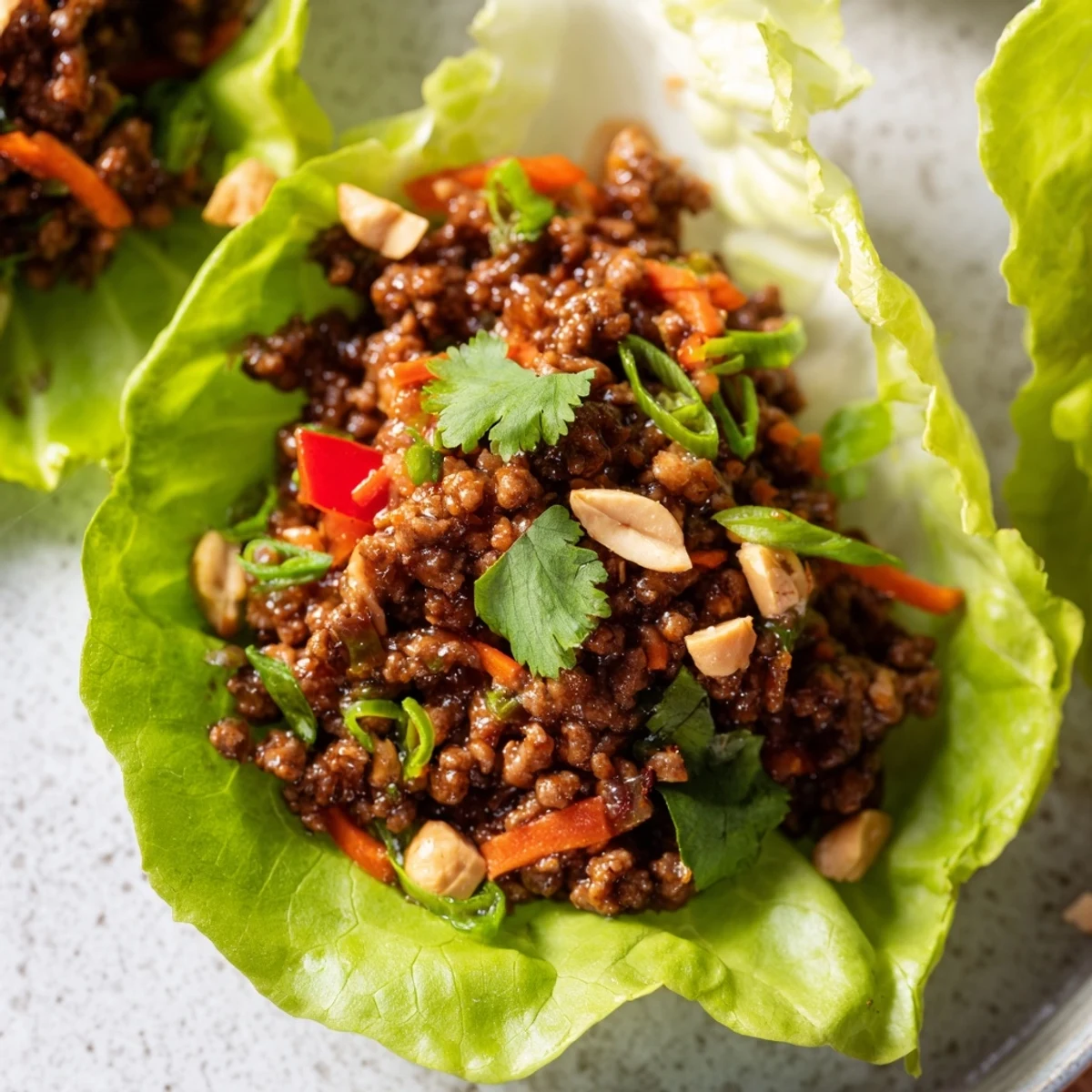 Freshly assembled Asian-inspired lettuce wraps featuring tender beef, crunchy veggies, and a glossy hoisin glaze, perfect for a light and flavorful meal.