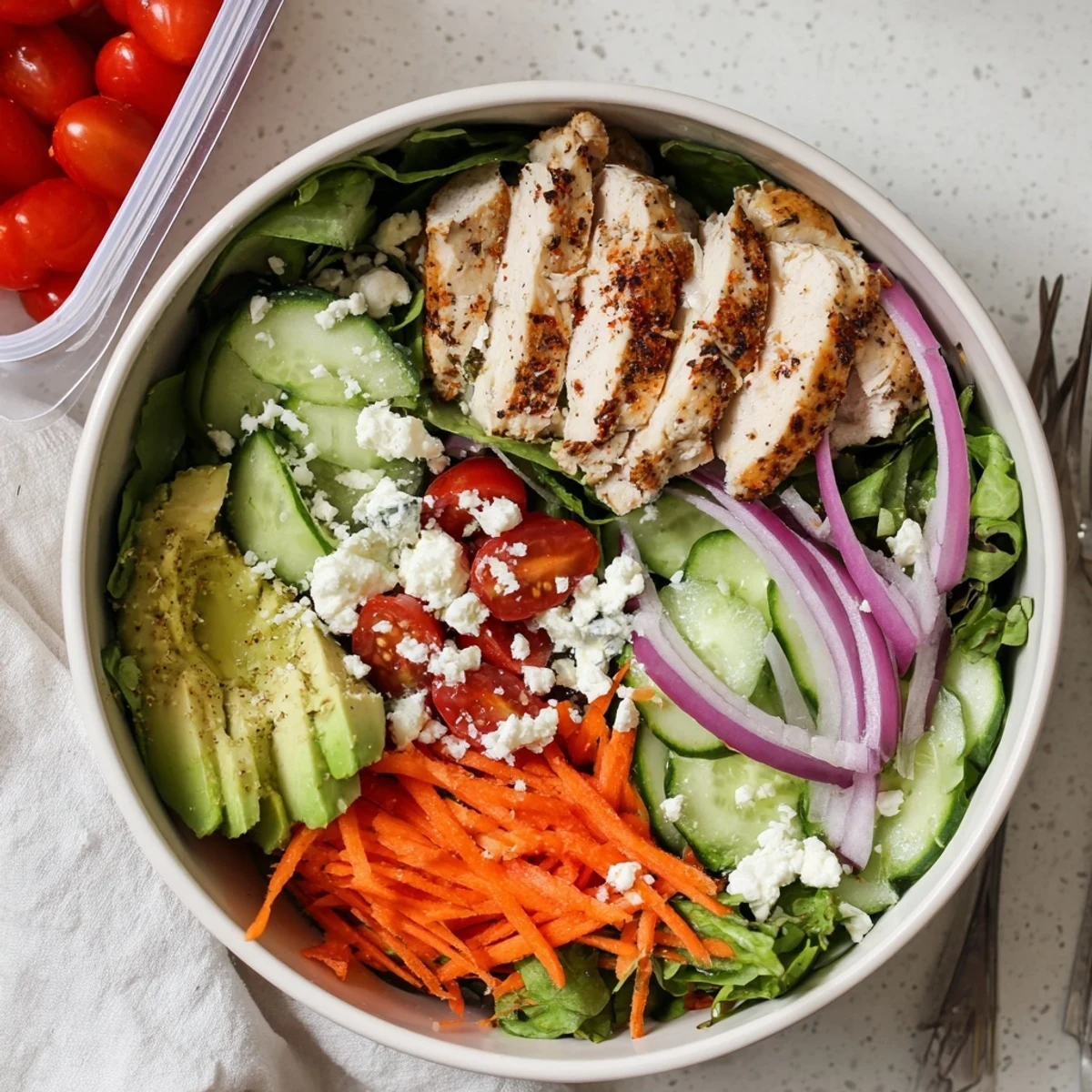 A close-up view shows grilled chicken breast, crisp romaine, and ripe avocado in a portable salad meal prep bowl.