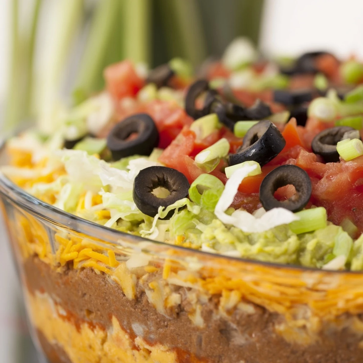 Freshly prepared Super Bowl Seven Layer Taco Dip, featuring bright guacamole and chunky salsa, is served with golden tortilla chips for easy dipping.