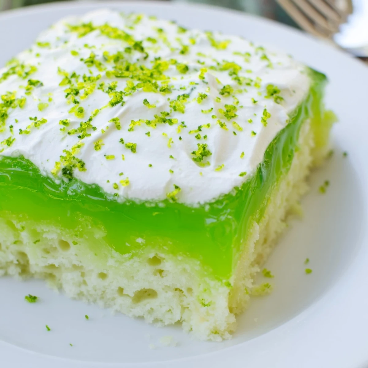 Moist St. Patrick's Day Lime Poke Cake squares with vibrant green gelatin soaking into the crumb and a fluffy whipped topping.