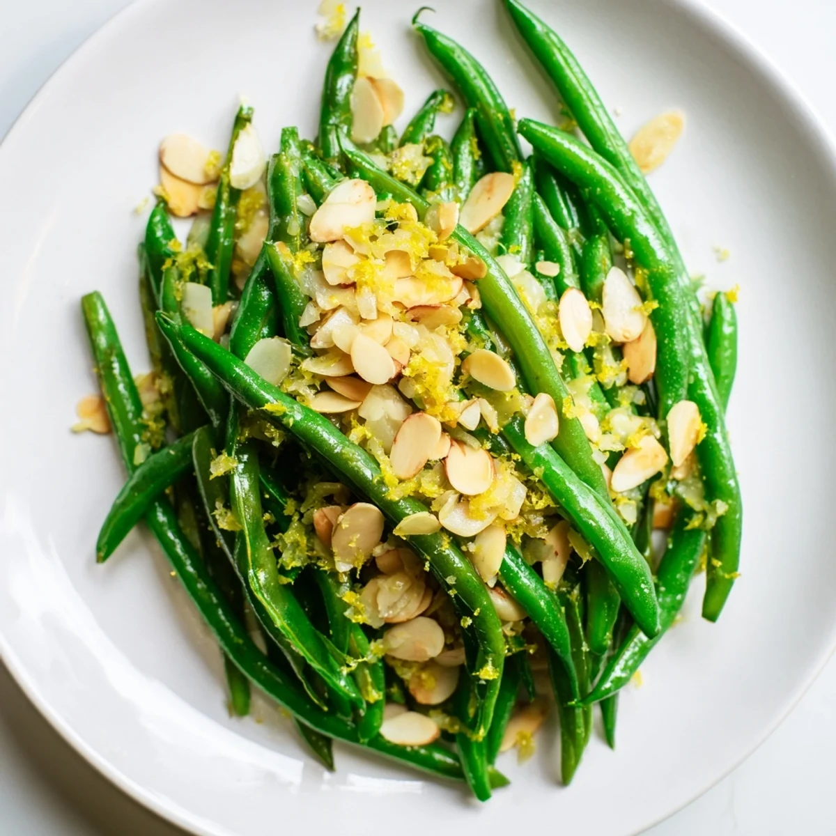 Close-up of green beans with lemon and almonds tossed with minced garlic, plated with a fresh lemon wedge garnish.