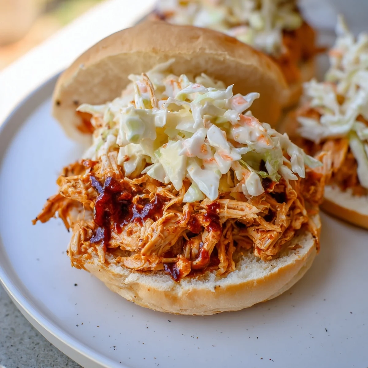 Freshly shredded Tailgate Pulled Chicken Sandwiches stacked high with creamy coleslaw on toasted buns.