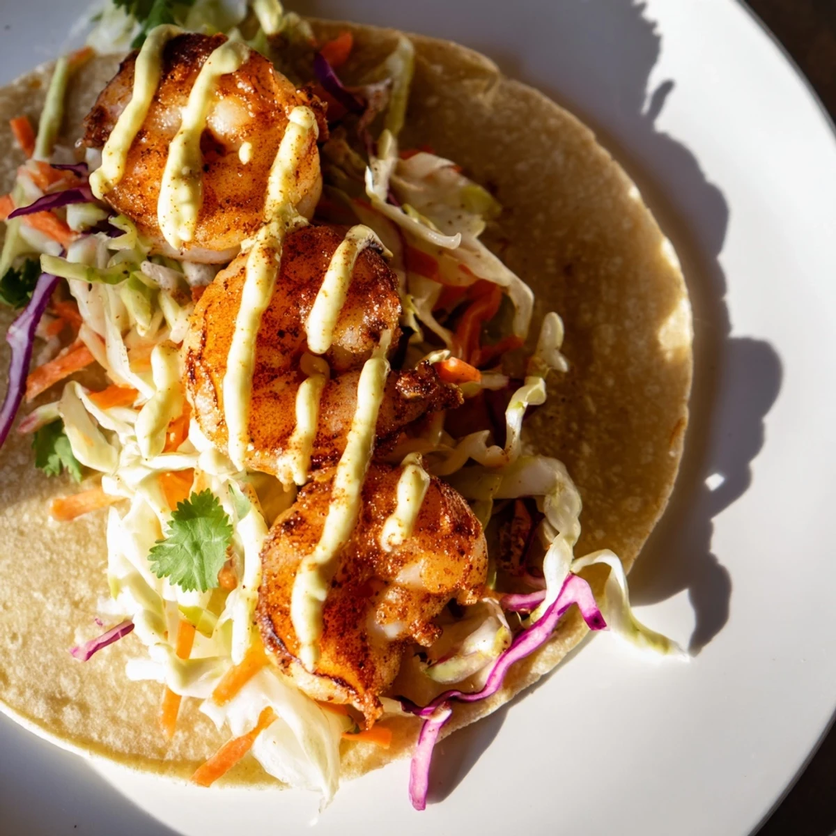 Plated Shrimp Tacos with Cabbage Slaw and Lime Crema in warm corn tortillas.