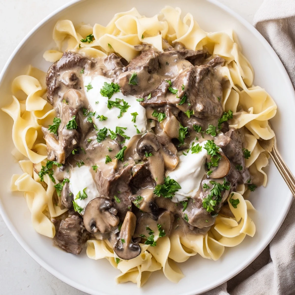 Steaming Beef Stroganoff with Egg Noodles in a creamy mushroom sauce, garnished with fresh parsley.