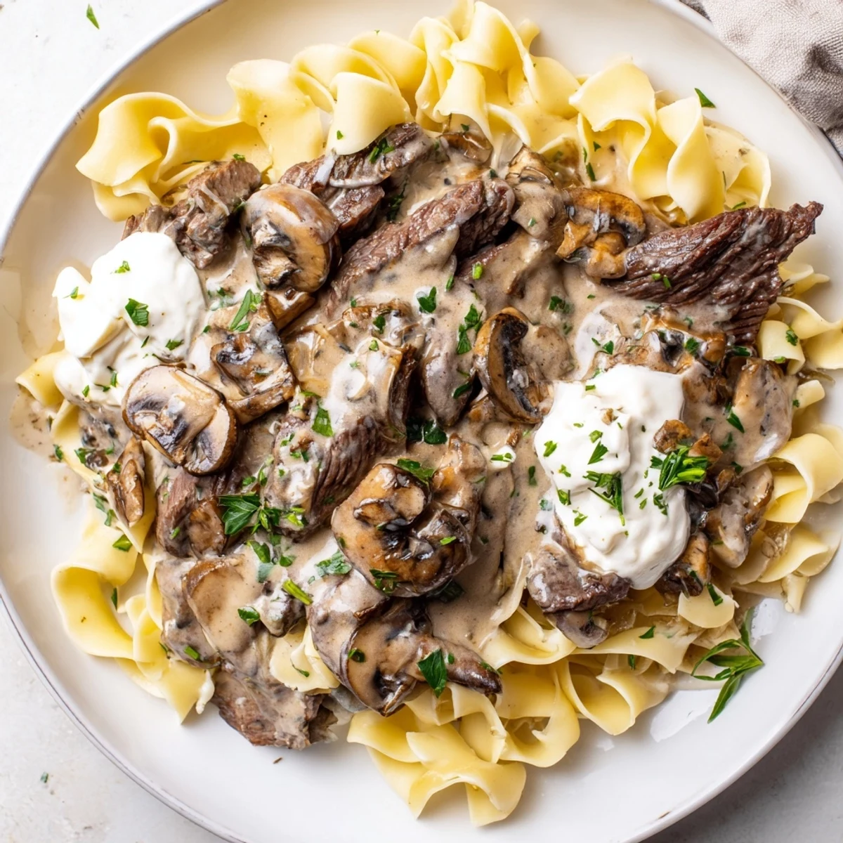 Beef Stroganoff with Egg Noodles plated with golden noodles and savory, creamy mushroom sauce.