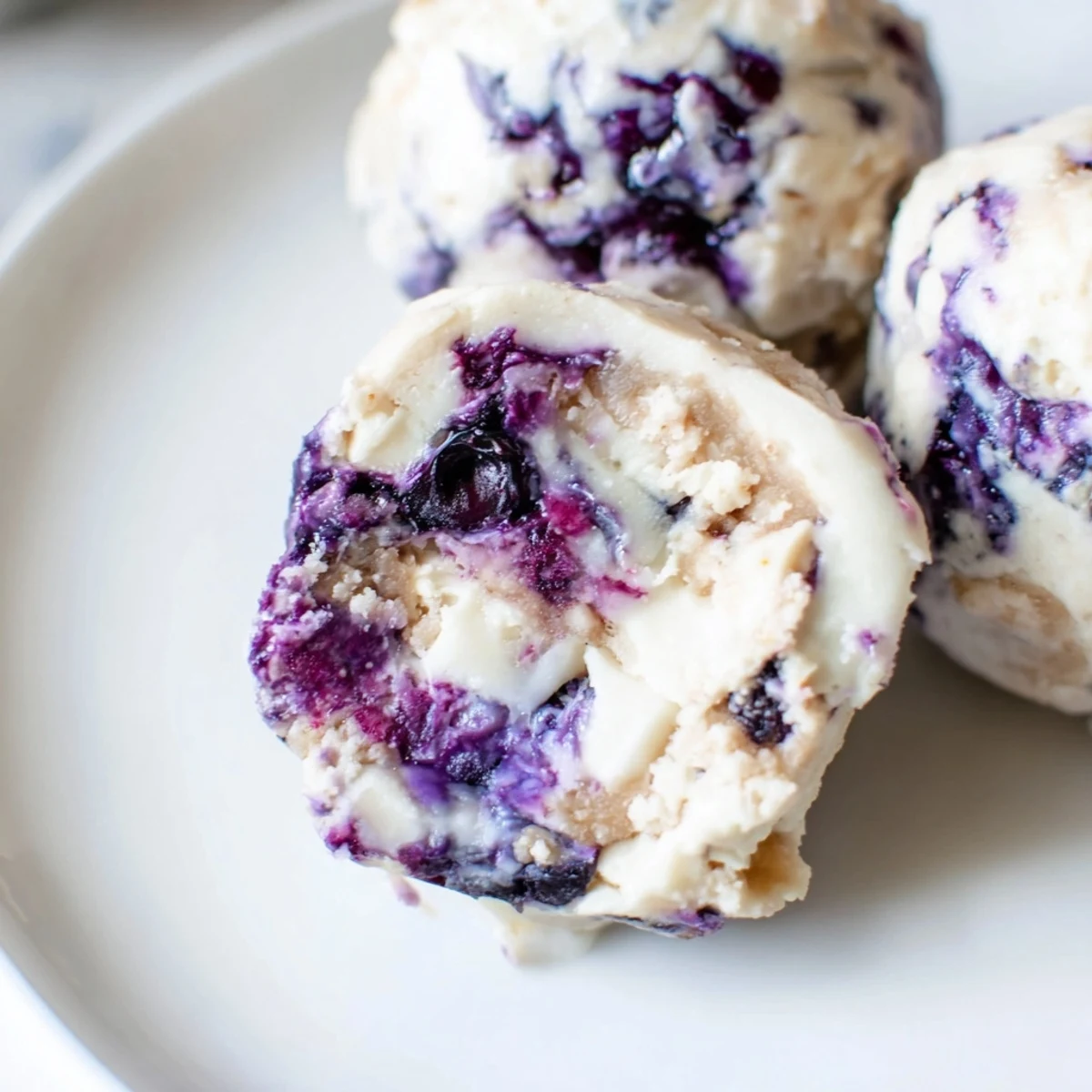 A close-up of Blueberry Cheesecake Protein Bites showing tangy cream cheese layers and vibrant blueberry compote swirls.