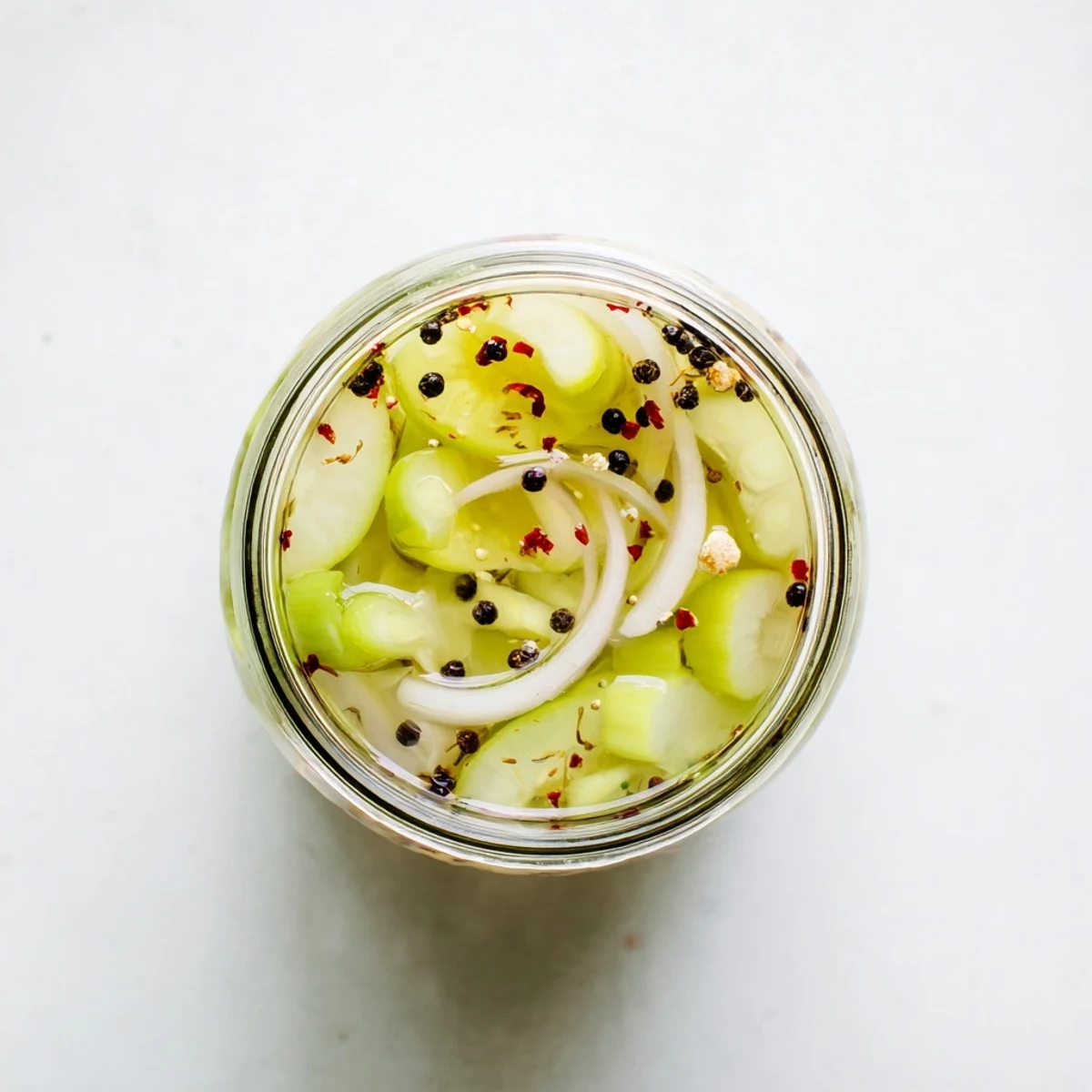 Brightly brined Quick Pickled Celery in a jar, showcasing crisp green stalks with mustard seeds and red pepper flakes for a tangy snack or salad topping.