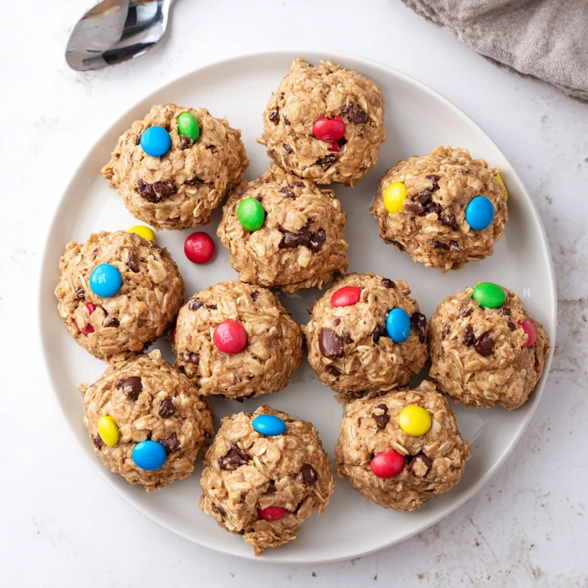 A close-up of Monster Cookie Protein Balls on a marble surface, showing chewy oats, chocolate chips, and colorful candy pieces.
