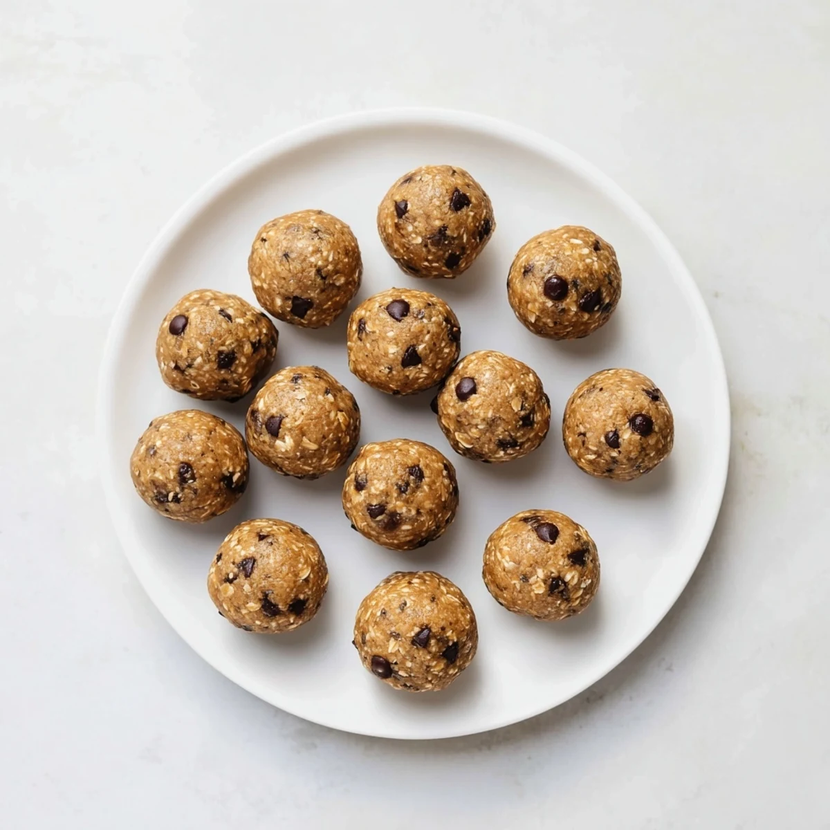 A close-up of green Mint Chocolate Chip Protein Balls rolled on a white plate with chocolate chips.