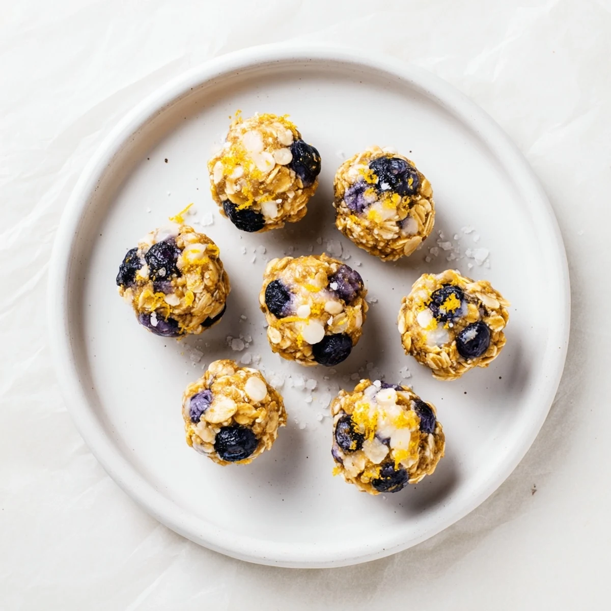 Freshly rolled Blueberry Cheesecake Protein Bites with creamy texture and vibrant blueberries on a rustic wooden board.