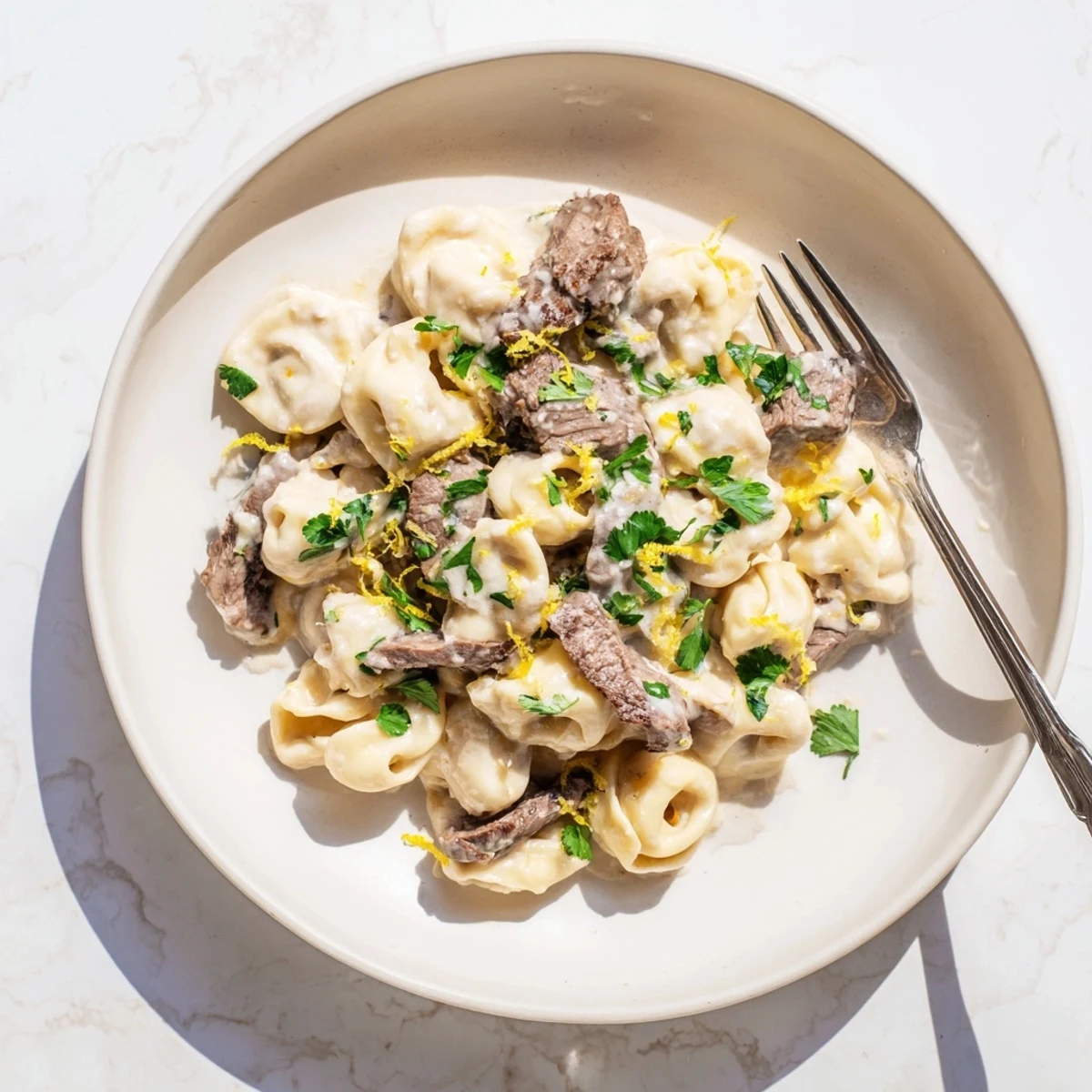 Sliced sirloin steak and cheese tortellini coated in rich creamy garlic-herb sauce with fresh parsley garnish