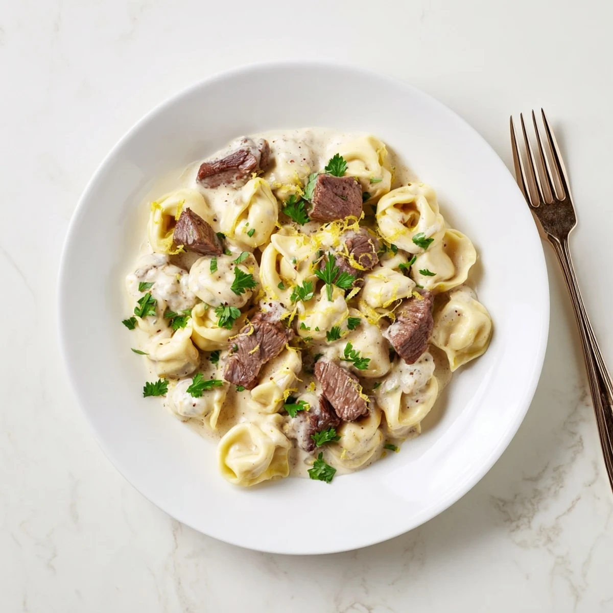 Steak tortellini pasta in velvety white Parmesan cream sauce topped with lemon zest and cracked black pepper
