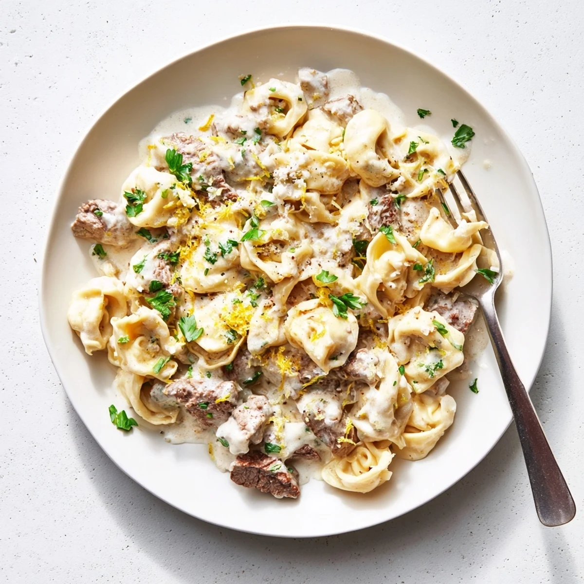 Tender seared beef pieces folded into tortellini swimming in a luscious garlic cream sauce with grated Parmesan