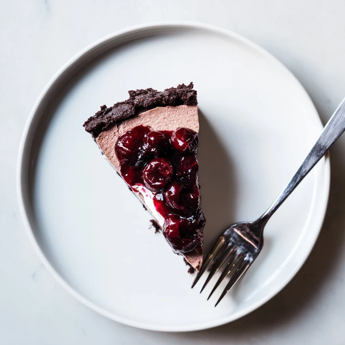 Creamy dark chocolate cherry cheesecake wedge with graham cracker crust and sweet cherry compote