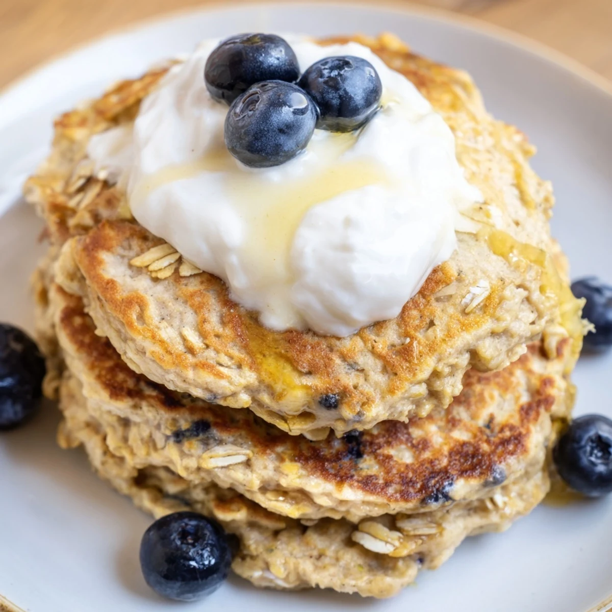 Golden stack of fluffy banana oatmeal pancakes topped with creamy Greek yogurt and fresh berries