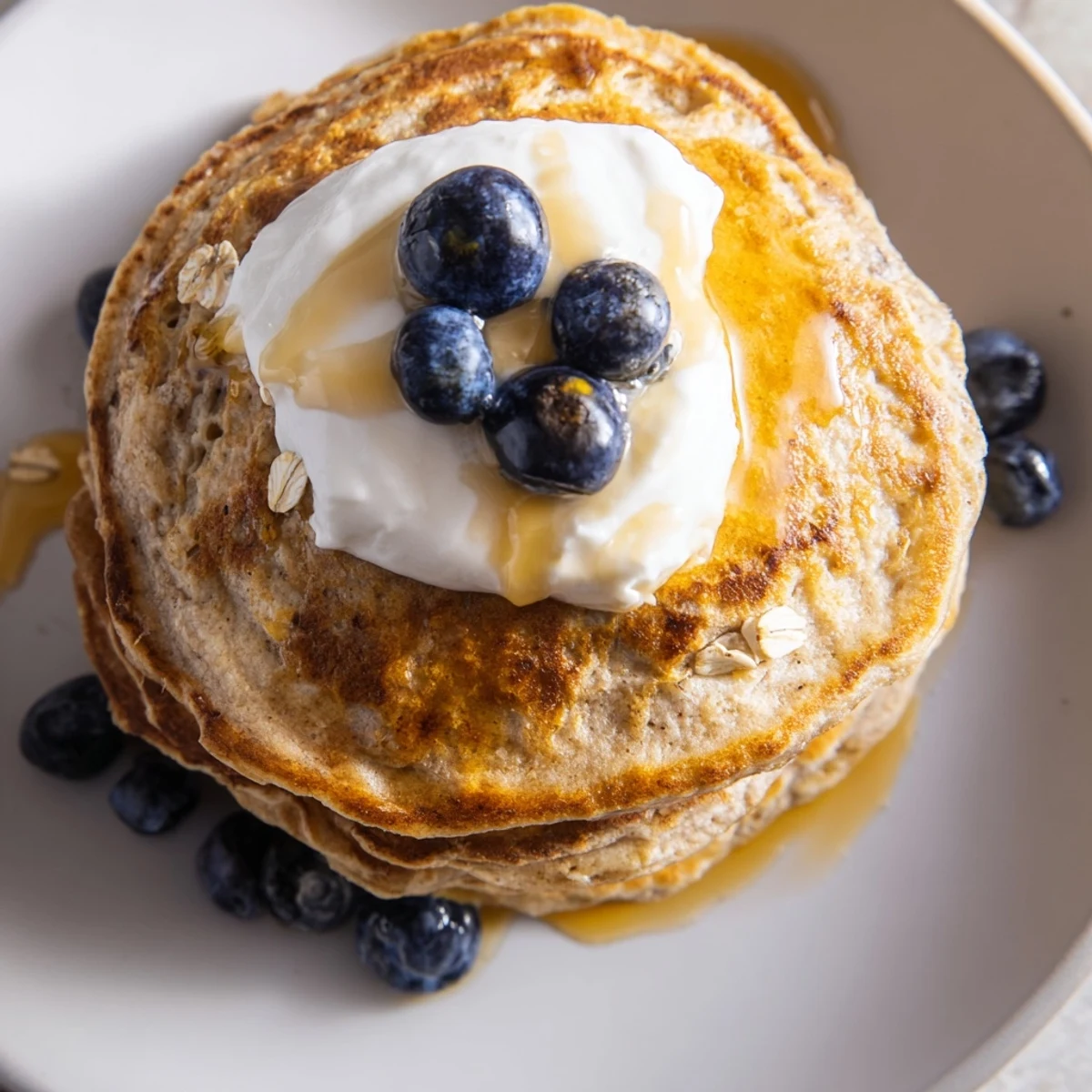 Homemade banana oatmeal pancakes with Greek yogurt drizzled with maple syrup on a white plate