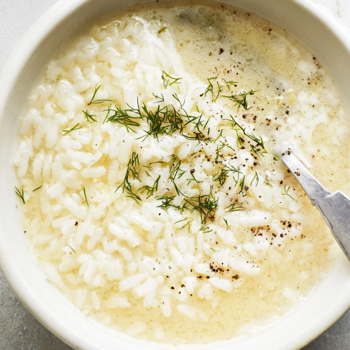 Close-up of classic Greek Egg and Lemon Soup showing smooth creamy texture with bright lemon accents and fluffy rice in a rustic ceramic bowl