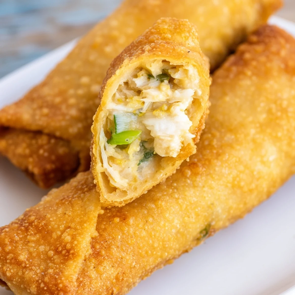 Crispy golden Crab Rangoon egg rolls plated on white background showcasing flaky pastry texture
