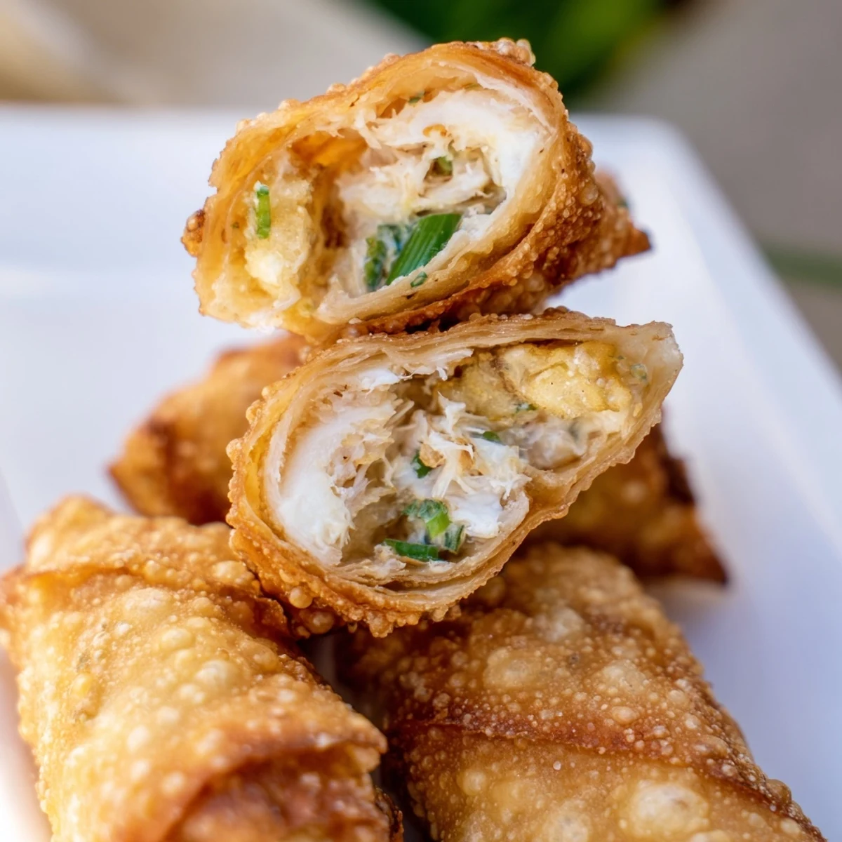 Plate of homemade Crab Rangoon egg rolls garnished with green onions and served with sweet chili sauce