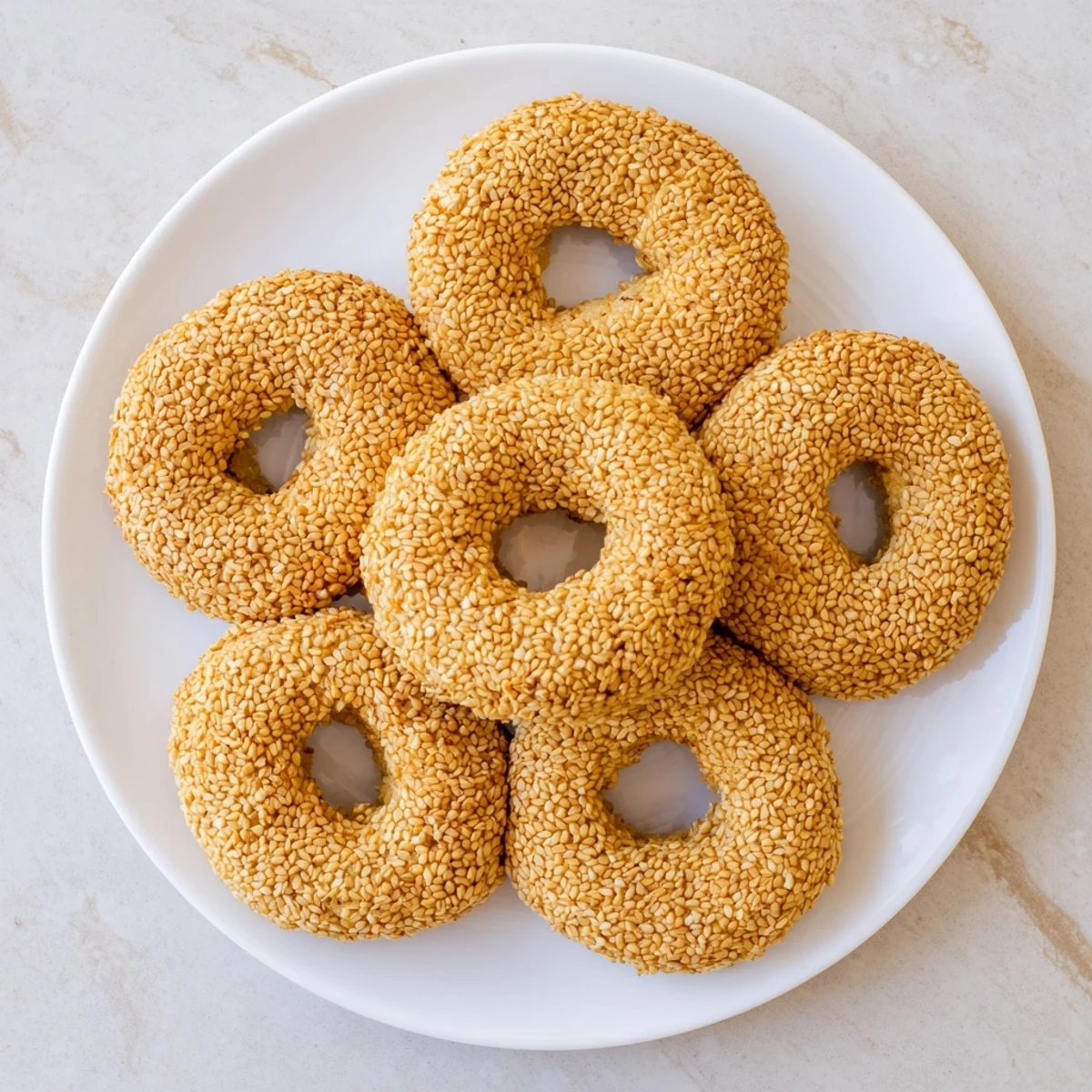 Golden sesame bread rings with crispy exterior and soft interior, freshly baked on a wire cooling rack.