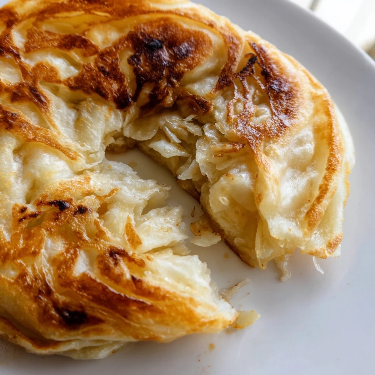 Hand-torn piece of flaky roti canai revealing tender layers inside