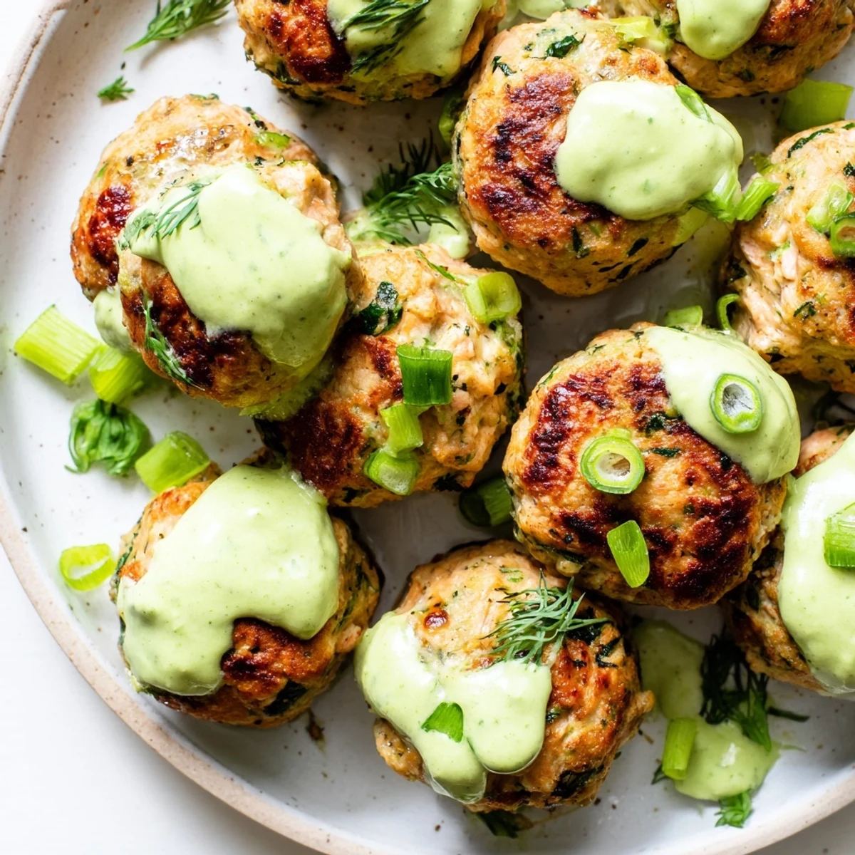 Close-up of tender baked salmon meatballs garnished with fresh dill and served alongside smooth zesty avocado sauce