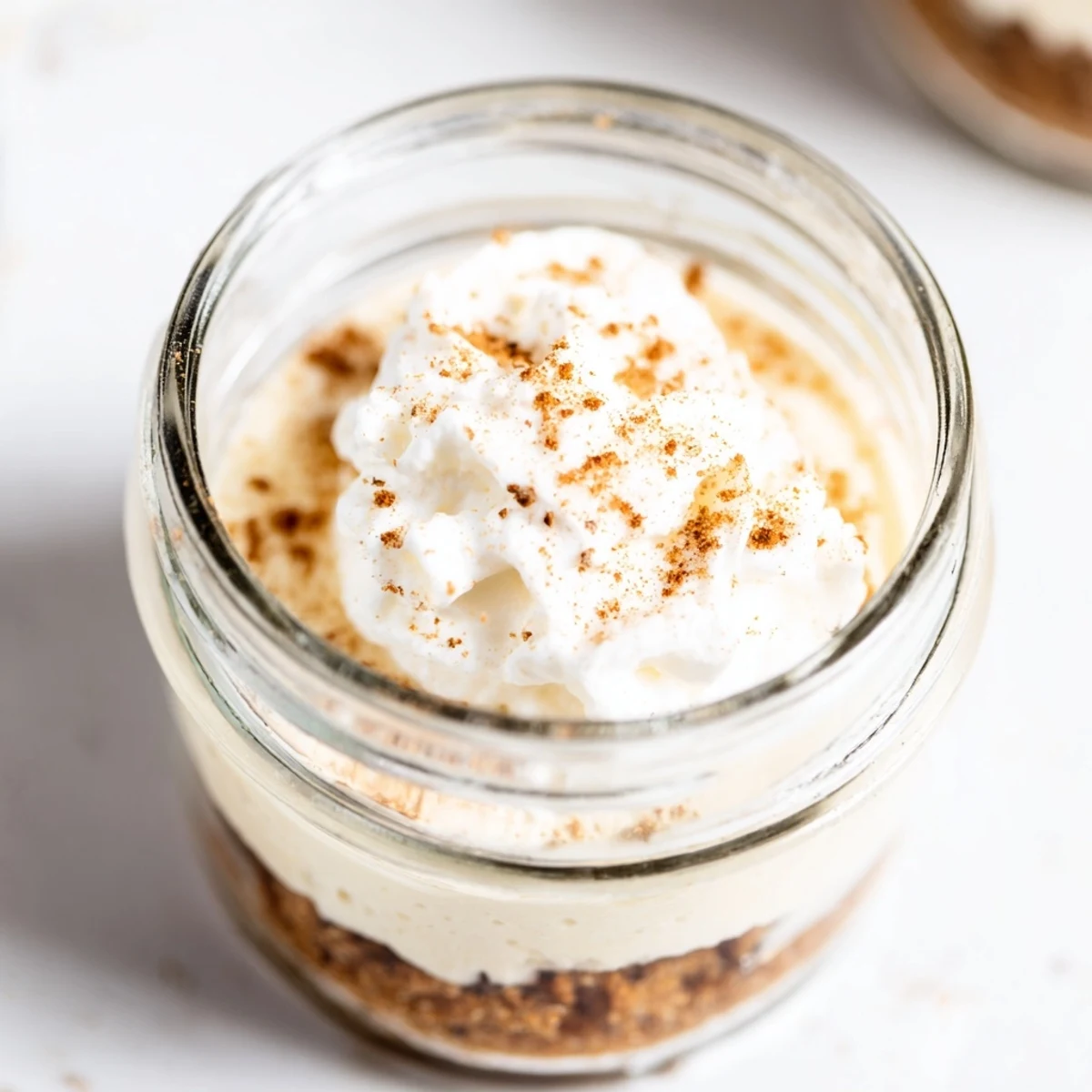 Individual glass jars layered with spiced cheesecake filling topped with fluffy whipped cream swirls
