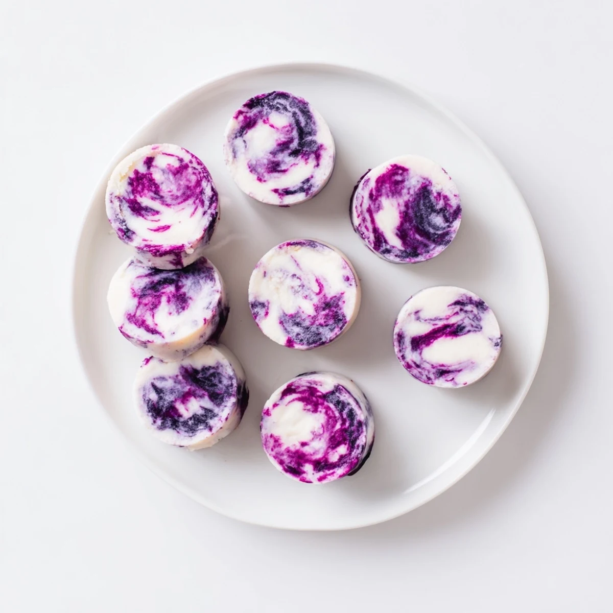 Creamy blueberry swirl yogurt bites arranged on a white plate with fresh berry garnish