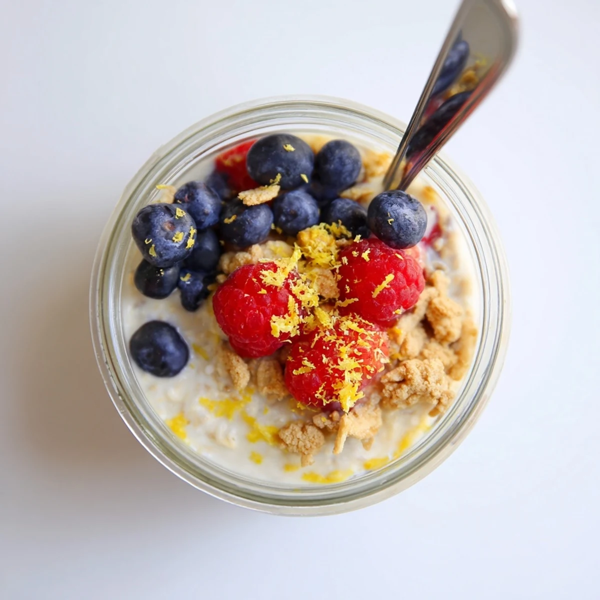 Spoonful of rich zesty lemon cheesecake overnight oats showing creamy texture with blueberries and crunchy graham cracker topping