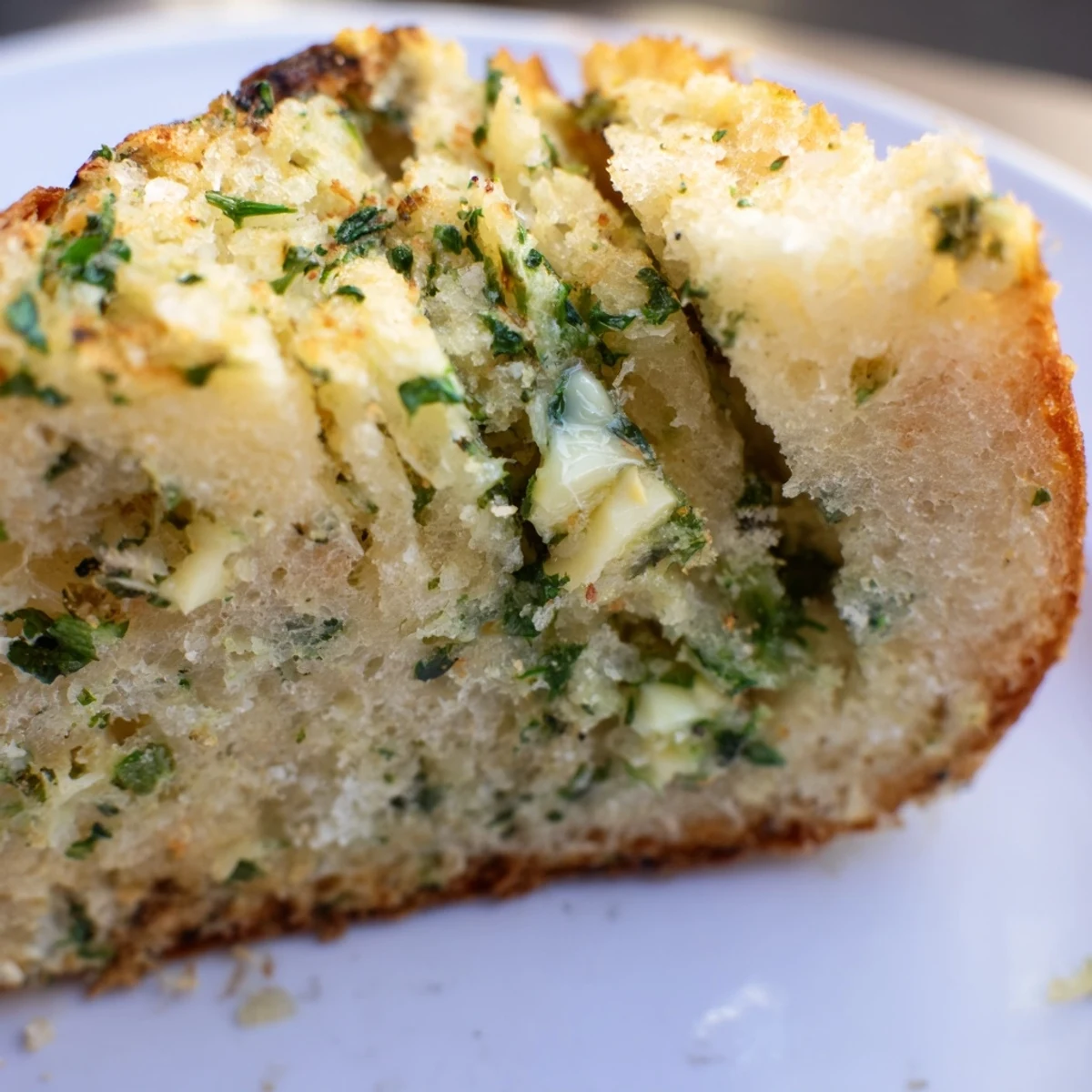 Warm slices of garlic and herb bread showing golden crust and green parsley flecks
