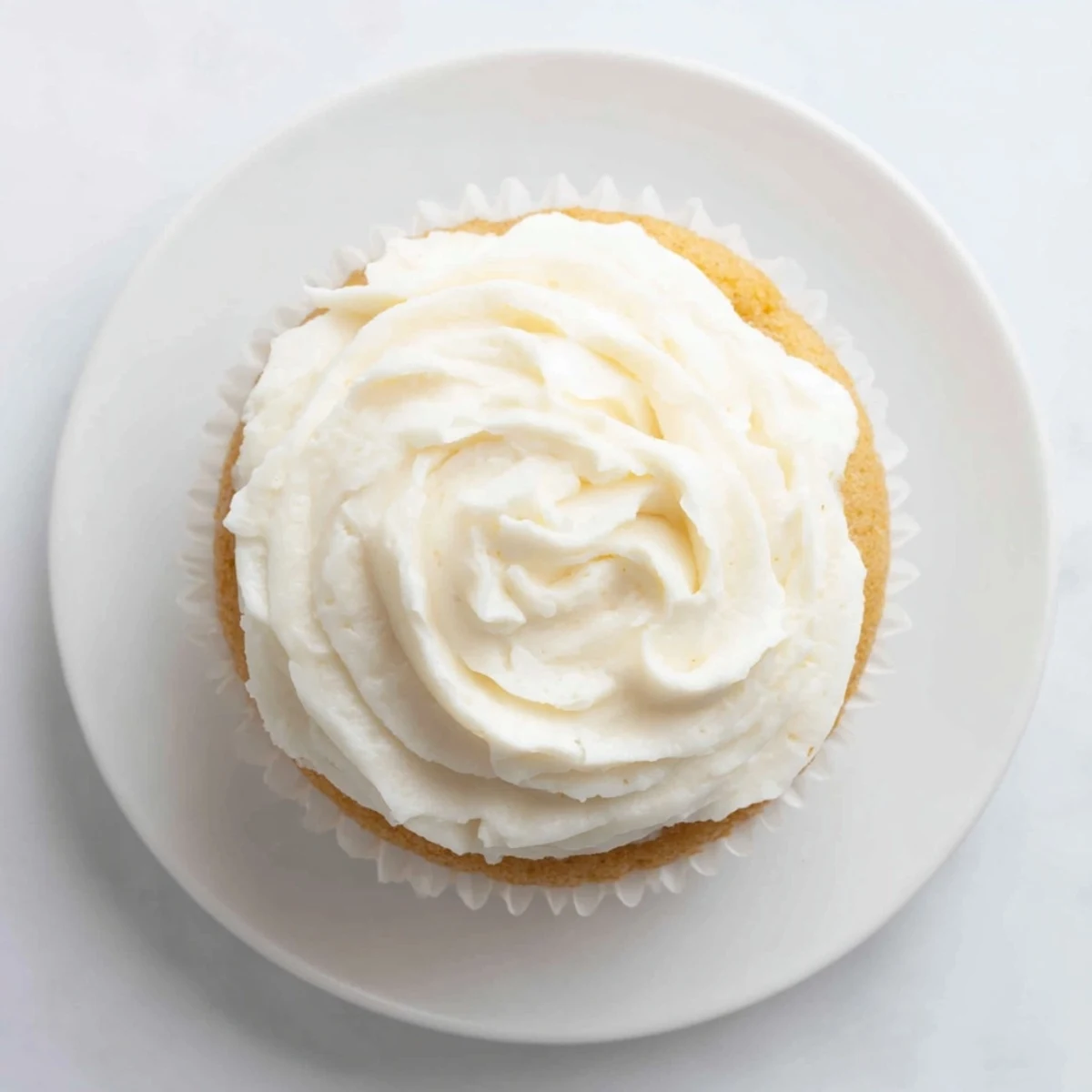 Golden vanilla cupcakes topped with fluffy white buttercream frosting and colorful sprinkles on a white plate