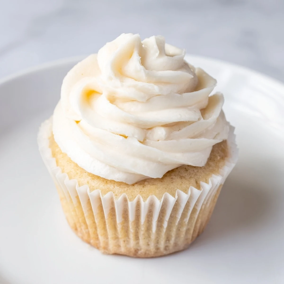 Baked vanilla cupcakes with smooth buttercream frosting piped high and decorated with sweet sprinkles