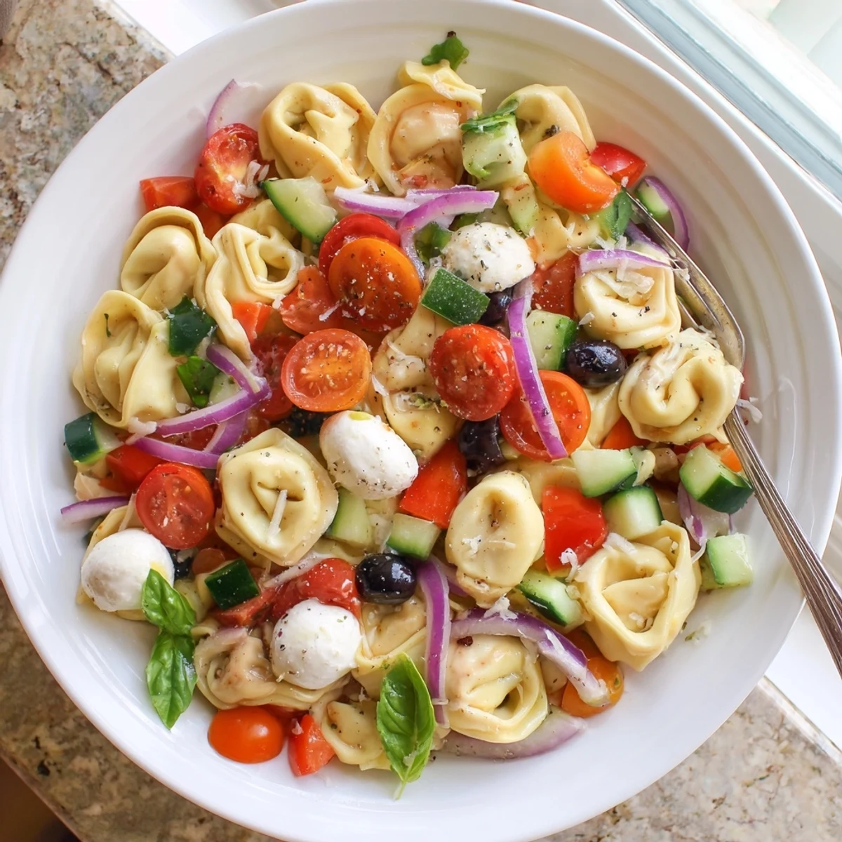 Colorful tortellini salad with cherry tomatoes, cucumber, and mozzarella tossed in zesty Italian dressing
