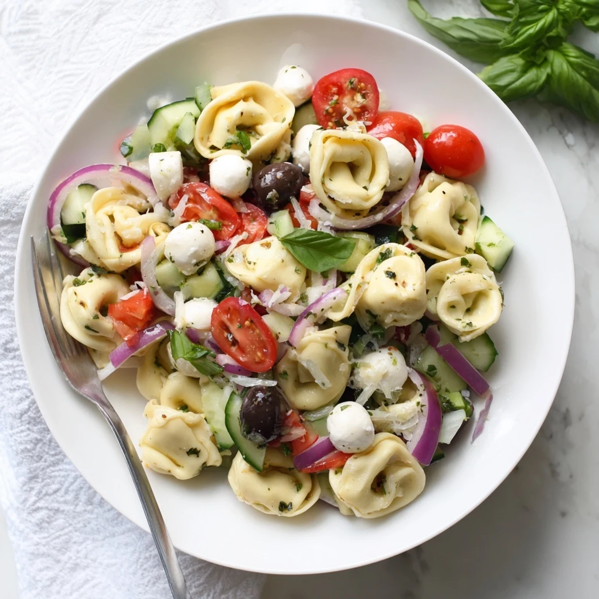 Creamy cheese tortellini salad topped with crisp vegetables and fresh basil in a vibrant bowl