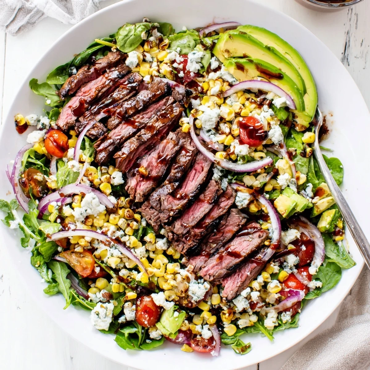 Golden grilled corn and creamy Gorgonzola crumble garnish a tender balsamic steak Gorgonzola salad with grilled corn on a wide platter.