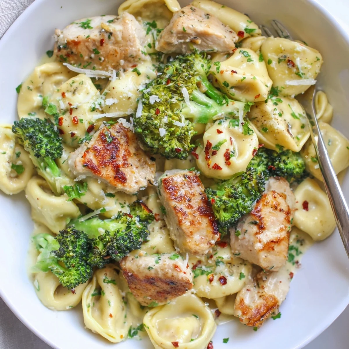 A bowl of Creamy Garlic Parmesan Tortellini Chicken Broccoli Recipe, juicy bites, bright broccoli