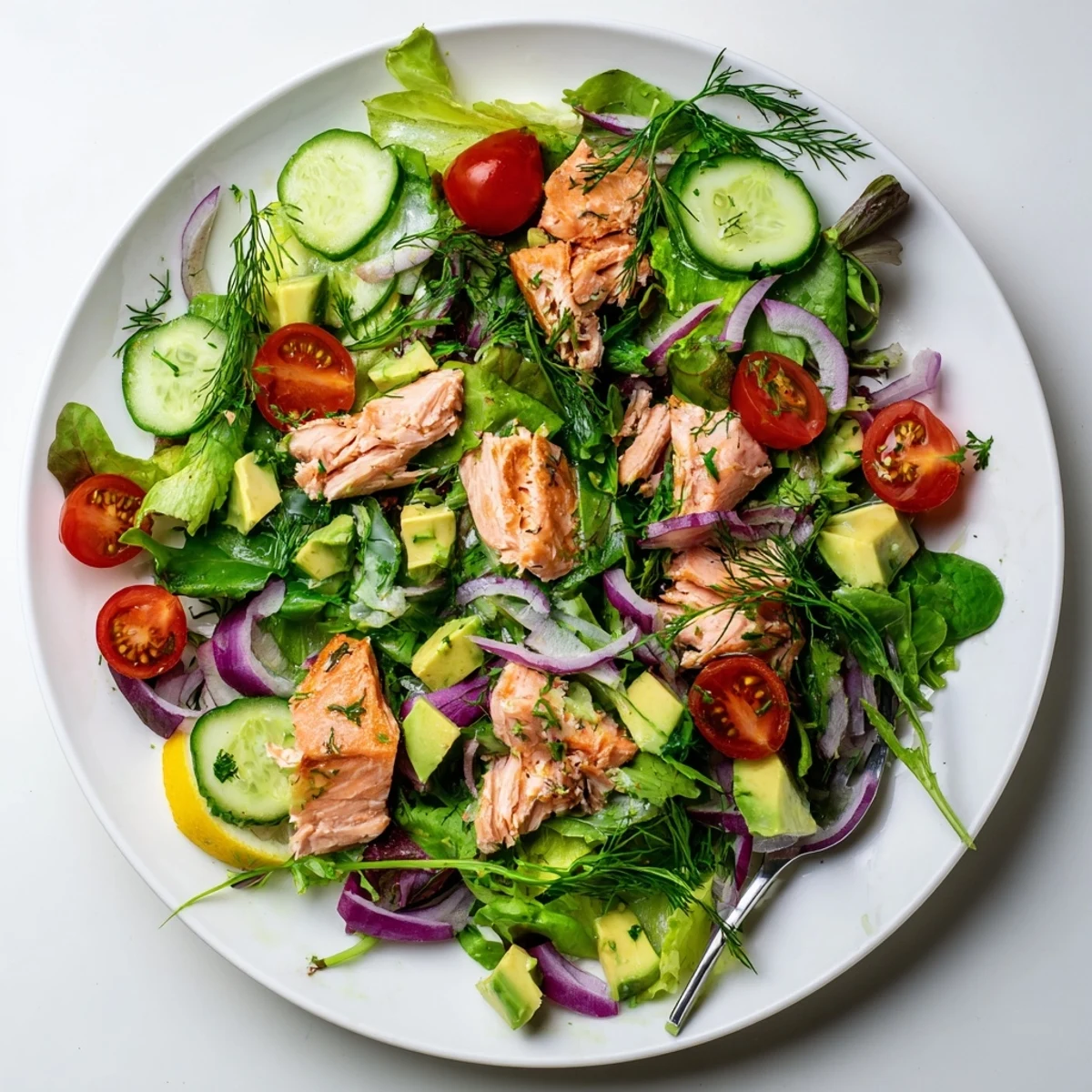 Golden baked salmon chunks atop fresh mixed greens with cherry tomatoes avocado crisp cucumber and red onion drizzled with zesty lemon-dill dressing