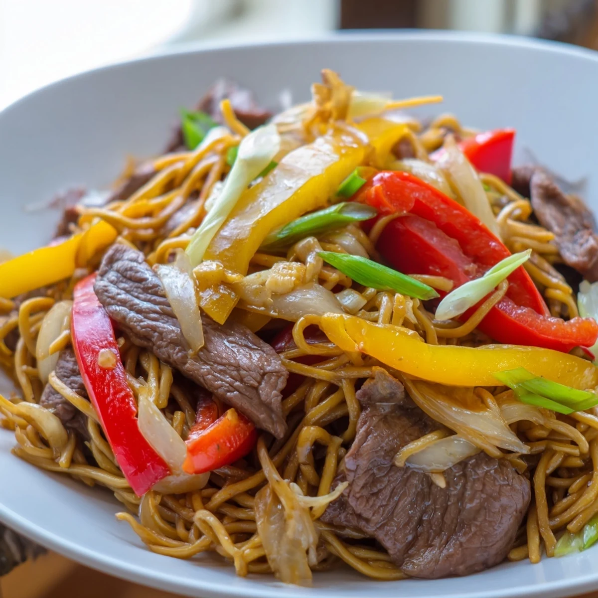 Steaming bowl of beef chow mein piled high with colorful peppers and caramelized onions