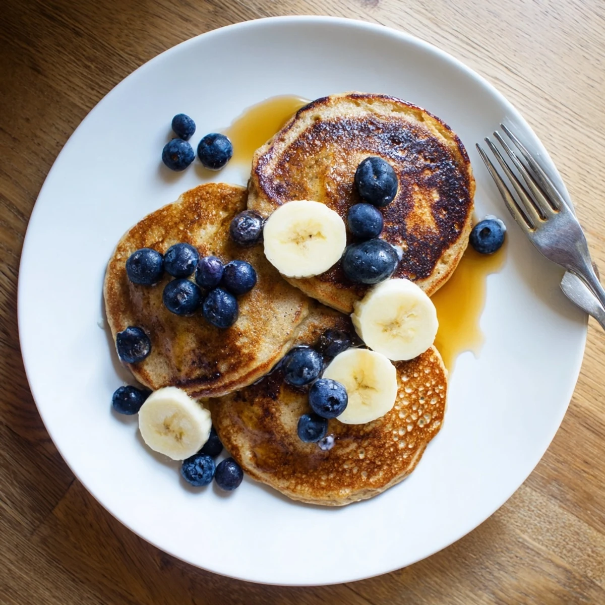 Golden stack of fluffy protein banana pancakes topped with fresh banana slices and maple syrup