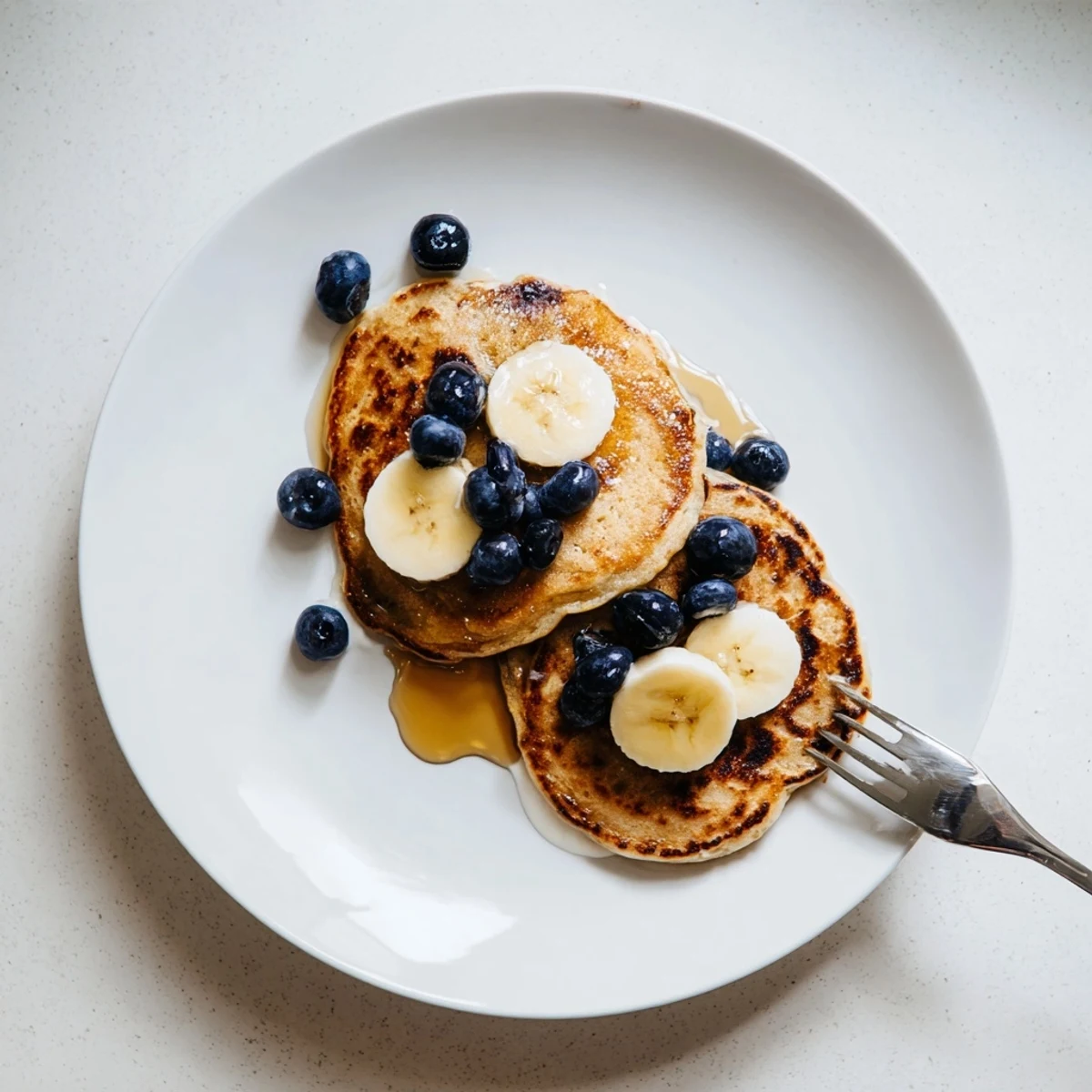 Thick American-style protein banana pancakes cooking in a skillet with visible golden-brown edges