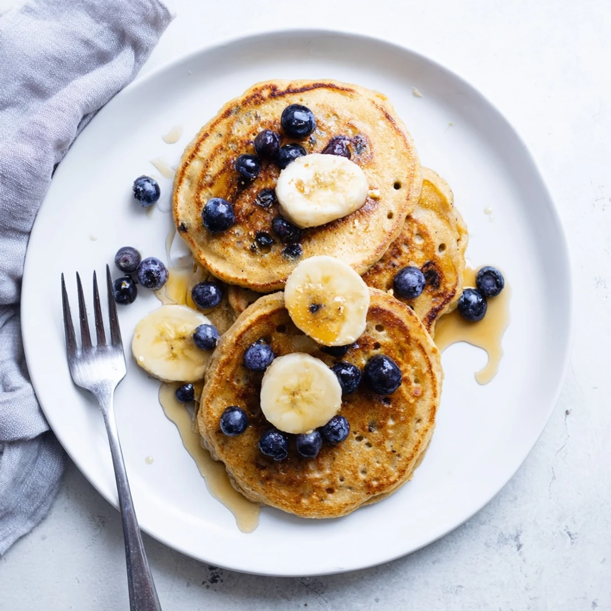 Plate of fluffy protein banana pancakes served with yogurt, berries, and a drizzle of honey