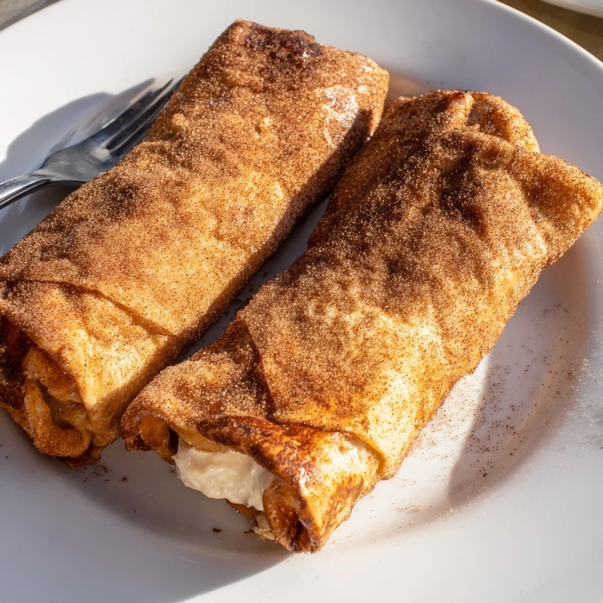 Golden crispy cheesecake chimichangas coated in warm cinnamon sugar on a rustic plate