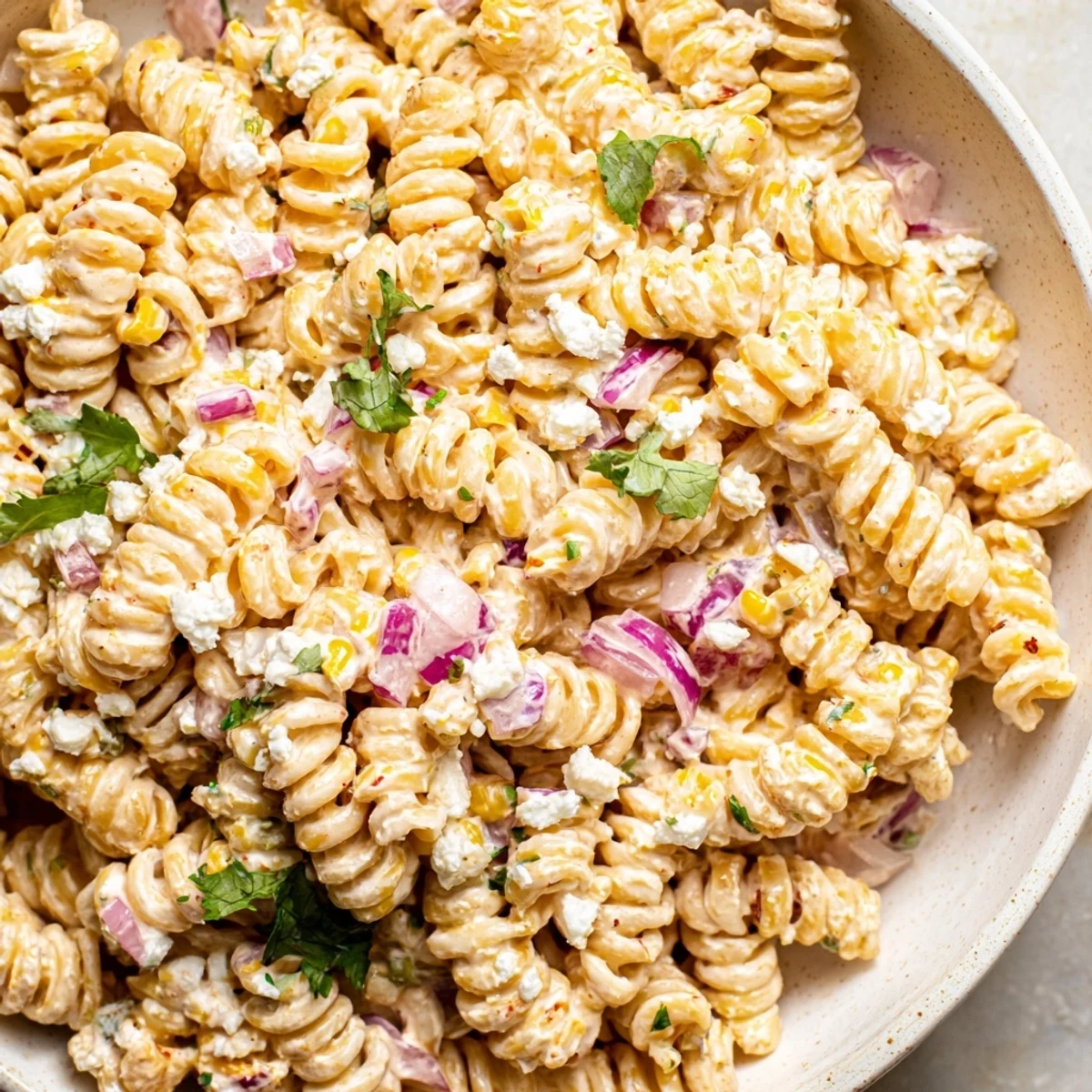 Vibrant elote pasta salad tossed in tangy lime dressing with crumbled cotija on top