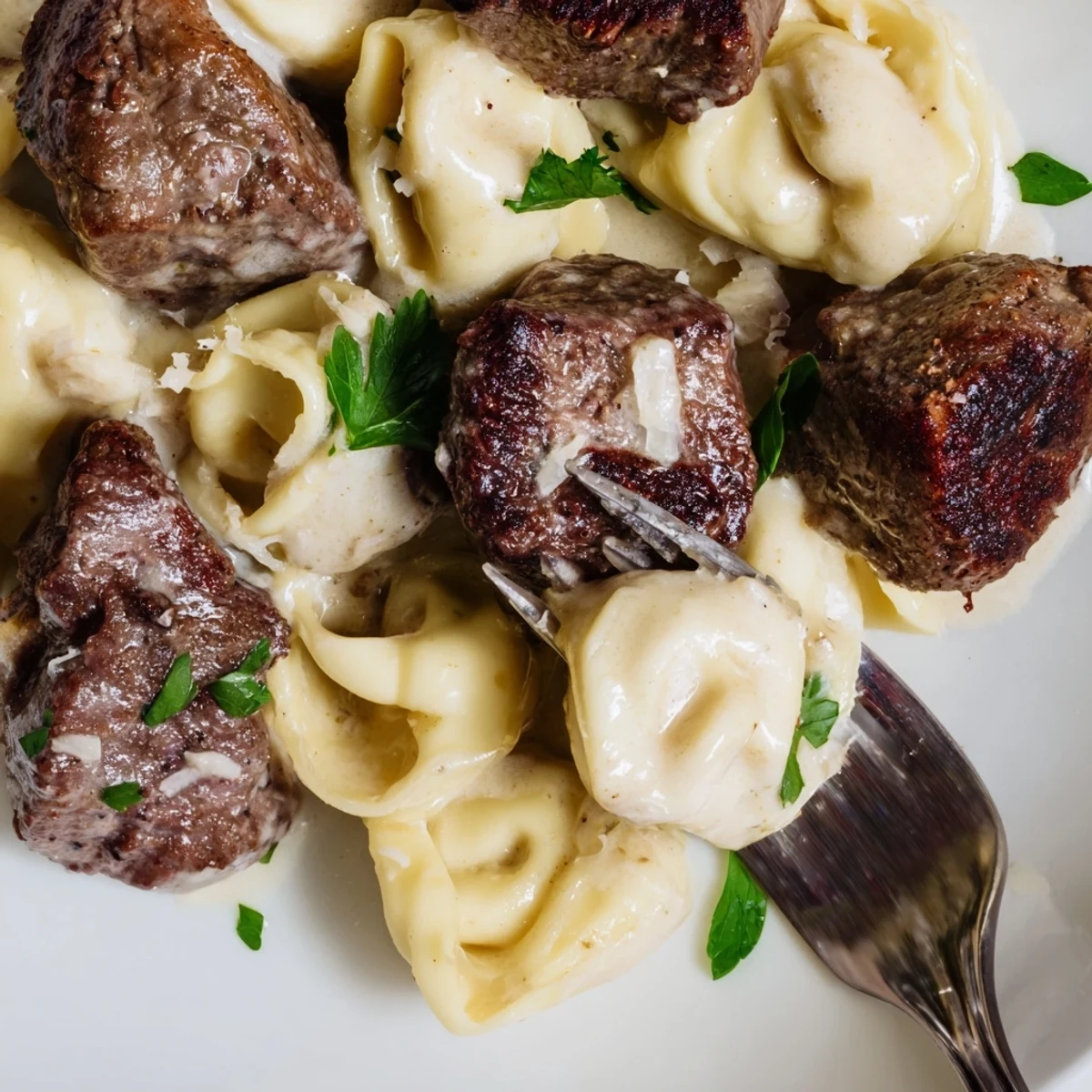 Close up of tender steak bites and tortellini tossed in garlic cream sauce.