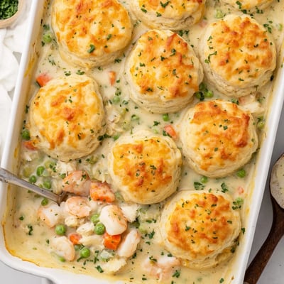 A close-up of seafood pot pie reveals chunky cod pieces and tender vegetables beneath the cheesy biscuit crust, ready to serve.