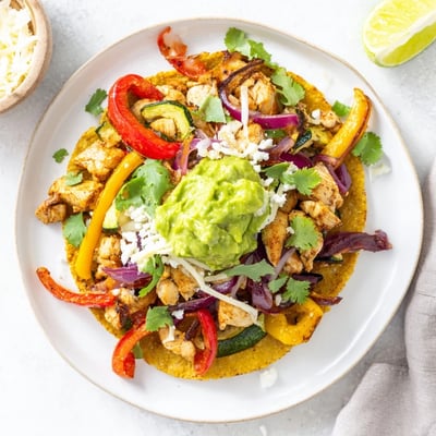 A vibrant plate of Chicken Veggie Tostadas With Guacamole, topped with fresh cilantro and lime wedges.  