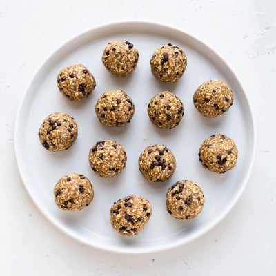 Twelve chilled Mint Chocolate Chip Protein Balls arranged in a circle on a marble counter with fresh mint.