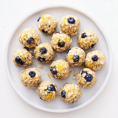A close-up view of Blueberry Cheesecake Protein Bites topped with extra blueberries and lemon zest for a bright flavor.