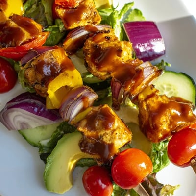 Juicy grilled BBQ chicken skewers served over fresh colorful summer greens.